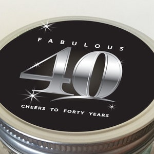 Op de afbeelding: Een zwarte deksel van een pot met een zilveren label waarop staat "Fabulous 40 Cheers to Forty Years". Het getal 40 is in een groot, zilveren lettertype met een glanzende, metallic afwerking. Er zijn kleine zilveren sterren rond het getal.
