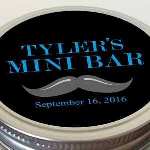 Op de afbeelding: Een zwarte deksel van een pot met een witte rand. De deksel heeft een blauw en wit etiket met de tekst "Tyler's Mini Bar" met daaronder een grijze snor. De datum "September 16, 2016" staat onder de snor.