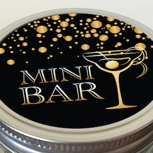Op de afbeelding: Zwarte en gouden deksel met een gouden martini-glas en de tekst "MINI BAR" op een zwarte achtergrond met gouden confetti.