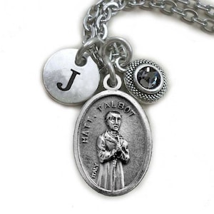 Peut inclure: Collier en argent avec un pendentif ovale en argent représentant une image religieuse d'un homme avec le texte "MATT. TALBOT ITALY". Le collier comporte également un charme en argent avec la lettre "J" et un charme en argent avec un strass noir.