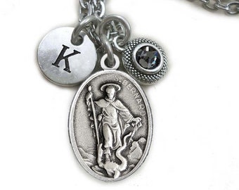 Può includere: Collana d'argento con un ciondolo di San Bernardo, un piccolo ciondolo rotondo con la lettera K e un ciondolo di cristallo nero.