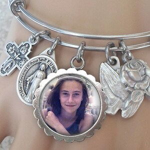 Op de afbeelding: Zilveren armband met verschillende bedels, waaronder een kruis, een fotobedel, een duif, een roos en een bedel met de tekst "O Maria, onbevlekt ontvangen, bid voor ons".