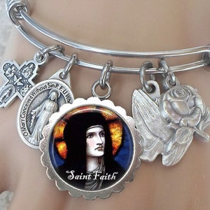 May include: A silver charm bracelet with multiple charms, including a cross, a rose, a dove, and a round charm with a stained glass image of Saint Faith. The bracelet is adjustable and has a spring clasp.