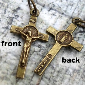 May include: A brass crucifix pendant with a depiction of Jesus Christ on the front and a Saint medal on the back. The pendant has a loop at the top for attaching to a chain.
