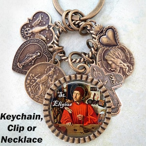 Puede incluir: Un llavero de bronce con varios dijes, incluyendo un corazón, una cruz y un dije redondo con una pintura de San Eligio. El texto "St. Eligius" es visible en el dije redondo. El llavero se puede usar como collar o clip.