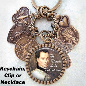 May include: A bronze keychain featuring a selection of charms, including a heart, a cross, and a round charm with a picture of St. Claude de la Colombière. The keychain can also be used as a clip or necklace.