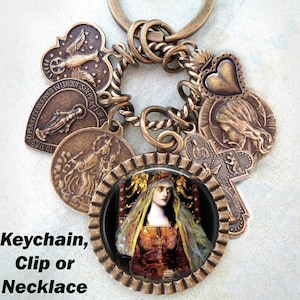 Puede incluir: Un llavero de bronce con una variedad de dijes, incluyendo un corazón, una cruz y un dije redondo con una imagen de una mujer con una corona. El texto "Oh María concebida sin pecado ruega por nosotros" está en uno de los dijes. El llavero también se puede usar como un clip o un collar.