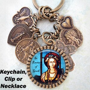 May include: A bronze keychain with a variety of charms, including a heart, a cross, and a stained glass image of St. Emma of Gurk. The keychain is attached to a twisted rope chain.