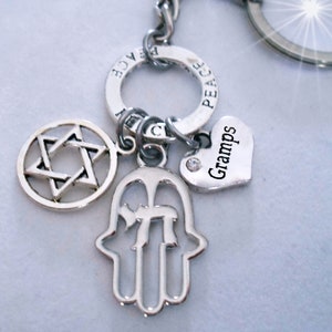 Puede incluir: Llavero de plata con una estrella de David, un amuleto de mano de Hamsa, un amuleto en forma de corazón con la palabra "Gramps" grabada y un amuleto de signo de paz.