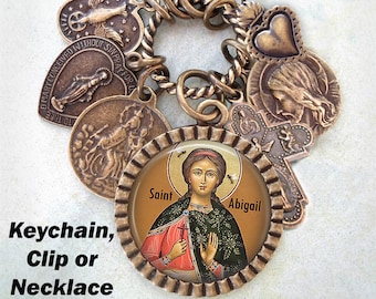 May include: A gold-toned charm bracelet with a variety of religious charms, including a heart, a cross, and a depiction of a saint. The bracelet is attached to a key ring.