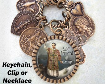 Può includere: Un portachiavi color bronzo con una varietà di ciondoli, tra cui un cuore, una croce e un ciondolo rotondo con un'immagine di San Bernardo di Menthon. Il testo "SAINT Bernard OF MENTHON" è stampato sul ciondolo rotondo.