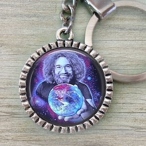 May include: A silver keychain with a round, glass charm featuring a color image of a man holding a blue and green globe. The background is a dark purple with white stars.