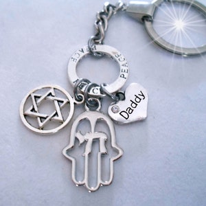 Puede incluir: Llavero de plata con un amuleto de la Estrella de David, un amuleto de la mano de Hamsa con la letra hebrea Jai, un amuleto de corazón con la palabra "Papá" grabada y un amuleto de signo de paz.