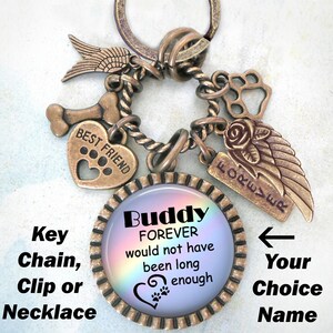 Puede incluir: Un llavero conmemorativo para mascotas de color bronce con un encanto iridiscente arcoíris que dice "Buddy FOREVER would not have been long enough". El encanto está rodeado de otros encantos, incluyendo un hueso, un corazón con huellas de patas, una huella de pata, una rosa y un ala.