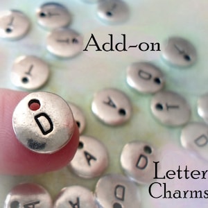 May include: Silver letter charms with a hole for attaching to jewelry. The charms are in the shape of a circle and have a letter 'D' stamped on them. The text 'Add-on Letter Charms' is visible in the image.
