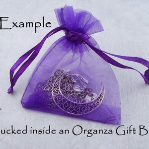 May include: Purple organza gift bag with a silver charm necklace inside. The charm is a crescent moon with the words "Sister of the Groom" on it.