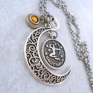 Puede incluir: Collar plateado del zodiaco Sagitario con un colgante de media luna con intrincados adornos. El collar incluye un dije redondo con el s&iacute;mbolo de Sagitario y un peque&ntilde;o dije redondo de piedra preciosa naranja. La cadena es de color plateado.