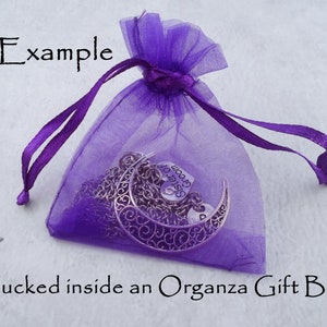 Op de afbeelding: Een paarse organza cadeauzak met een zilveren ketting met bedel. De bedel is een halve maan met de tekst "Zuster van de Bruidegom" erop.