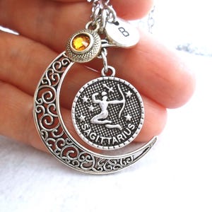 Puede incluir: Collar plateado del signo zodiacal Sagitario con un dije de media luna y un colgante redondo con un arquero. El collar incluye un peque&ntilde;o dije con una inicial y una gema amarilla. El dise&ntilde;o es intrincado y detallado.