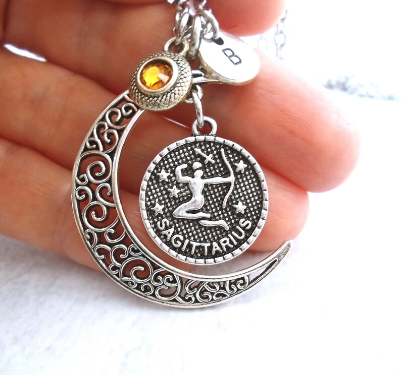 Puede incluir: Collar plateado del signo zodiacal Sagitario con un dije de media luna y un colgante redondo con un arquero. El collar incluye un peque&ntilde;o dije con una inicial y una gema amarilla. El dise&ntilde;o es intrincado y detallado.