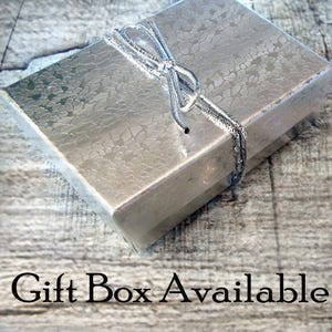 May include: A silver gift box with a silver ribbon tied in a bow. The box is sitting on a wooden surface. Gift Box Available.
