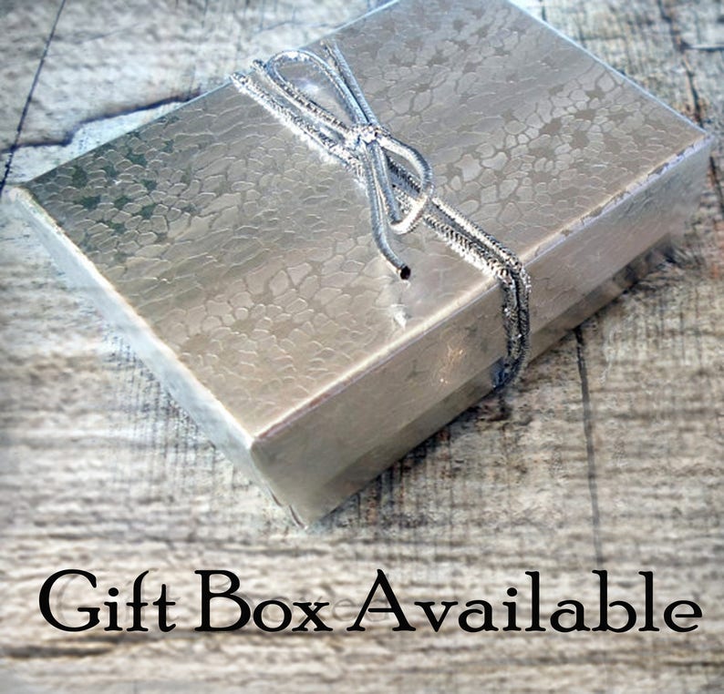 May include: A silver gift box with a silver ribbon tied in a bow. The box is sitting on a wooden surface. Gift Box Available.
