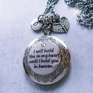 May include: Silver-toned locket necklace with a chain. The round locket has a floral border and a crystal accent. The text inside reads "I will hold You in my heart until I hold you in heaven." Includes a charm with the letter "D" and a heart-shaped wing charm.