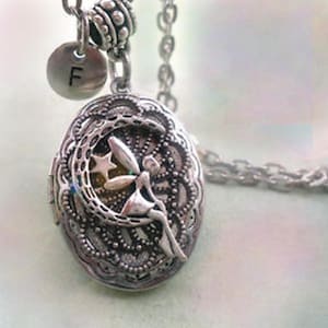 May include: A silver locket necklace with a crescent moon and fairy design. The locket has a delicate filigree pattern and a small initial charm that says "F".