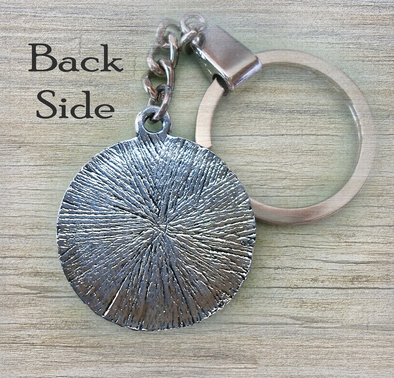 May include: Silver-toned metal keychain with a round, textured charm and a silver-toned metal ring. The back of the charm is visible.