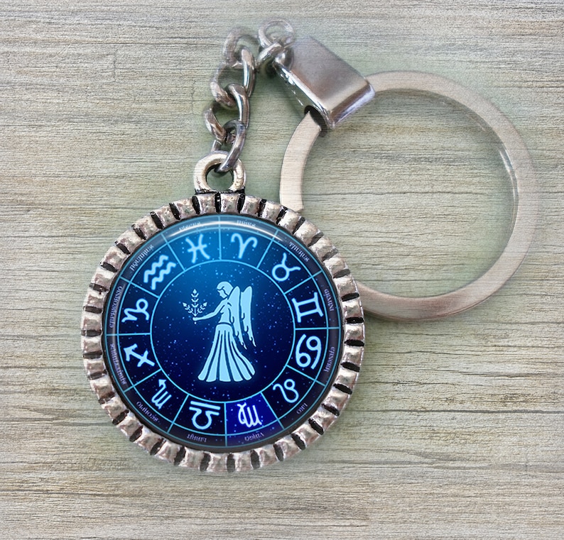 May include: Silver keychain with a blue and white circular charm featuring the astrological sign Virgo and the zodiac wheel. The charm has a silver border with a textured edge.