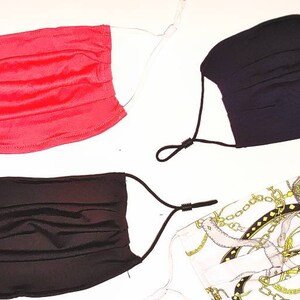 May include: Four face masks, two black, one red, and one white with a gold chain pattern. The masks are pleated and have elastic ear loops.