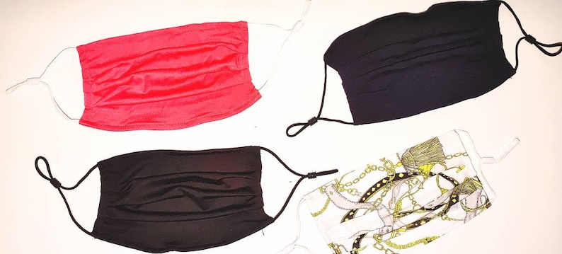 May include: Four face masks, two black, one red, and one white with a gold chain pattern. The masks are pleated and have elastic ear loops.