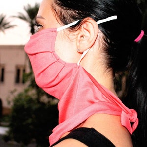 May include: A pink face mask with white straps, worn around the neck and tied at the back. The mask is made of a soft, stretchy fabric.