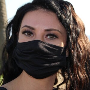 May include: A woman with long, dark brown hair is wearing a black face mask. She is looking at the camera with her eyes visible.