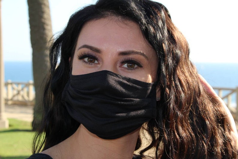 May include: A woman with long, dark brown hair is wearing a black face mask. She is looking at the camera with her eyes visible.