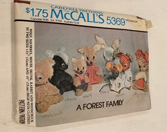 Könnte beinhalten: Vintage McCall's 5369 Schnittmusterumschlag. Das Schnittmuster enthält Anleitungen zur Herstellung von Stofftieren, darunter ein Wolf, ein Eichhörnchen, eine Maus, ein Stinktier, ein Kaninchen und ein Murmeltier, jeweils etwa 25 cm bis 32 cm groß. Der Umschlag trägt die Aufschrift "A FOREST FAMILY".