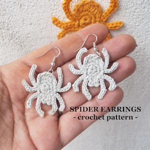 May include: A pair of crocheted spider earrings with silver hooks. The earrings are white and have a detailed design. The text "SPIDER EARRINGS - crochet pattern -" is visible below the earrings.