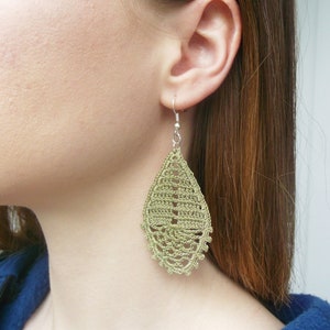 May include: A pair of green crochet earrings in a teardrop shape. The earrings are made with a delicate, intricate pattern.