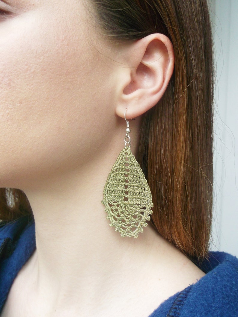 May include: A pair of green crochet earrings in a teardrop shape. The earrings are made with a delicate, intricate pattern.