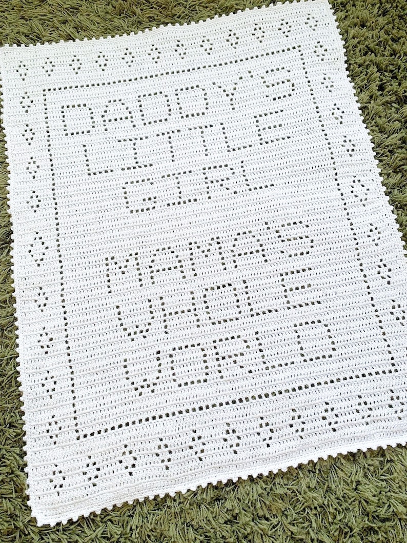 K&ouml;nnte beinhalten: Wei&szlig;e geh&auml;kelte Babydecke mit einem zarten Muster aus Blumen und Bl&auml;ttern. Die Decke hat einen gewellten Rand.