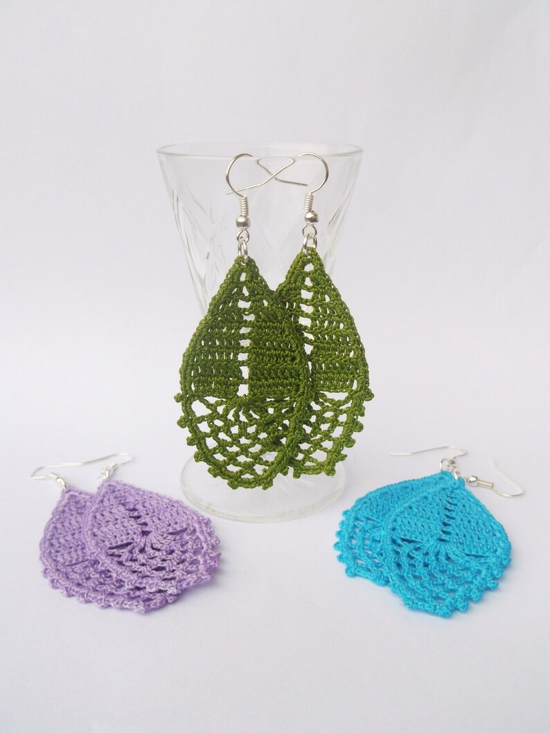 May include: Three pairs of crocheted earrings in green, purple, and blue. The earrings are teardrop shaped and have a delicate, lacy design.