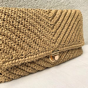 May include: A woven straw clutch bag with a gold clasp. The bag has a chevron pattern on the flap and a textured weave. The neutral colour makes it a versatile accessory.