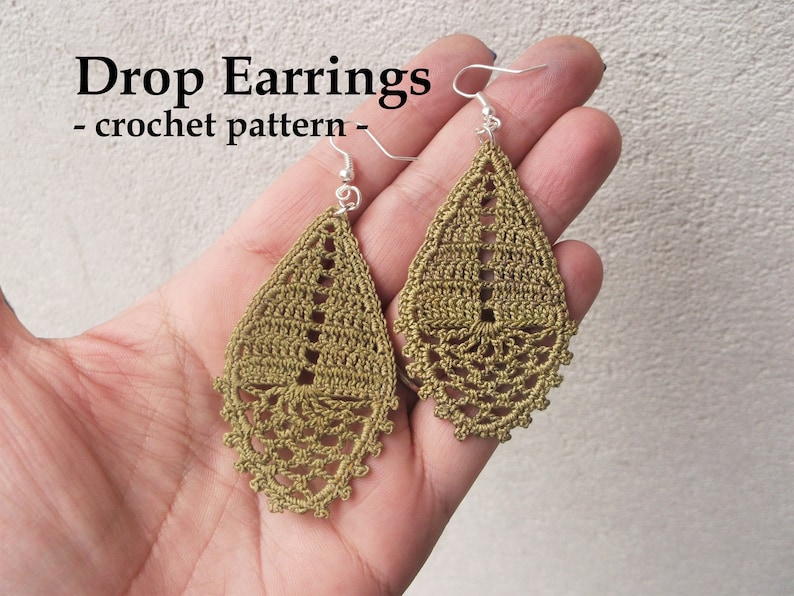 May include: A pair of crocheted drop earrings in a muted green color. The earrings are teardrop shaped and feature a delicate lace pattern. The earrings are hanging from silver hooks.
