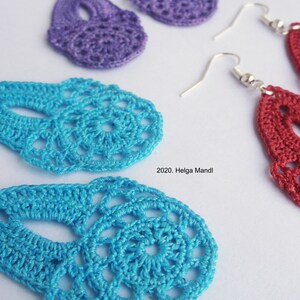Puede incluir: Primer plano de pendientes de ganchillo hechos a mano en tonos morado, turquesa y rojo. Los pendientes tienen un dise&ntilde;o delicado y calado con ganchos plateados. La imagen incluye el texto "2020. Helga Mandl".