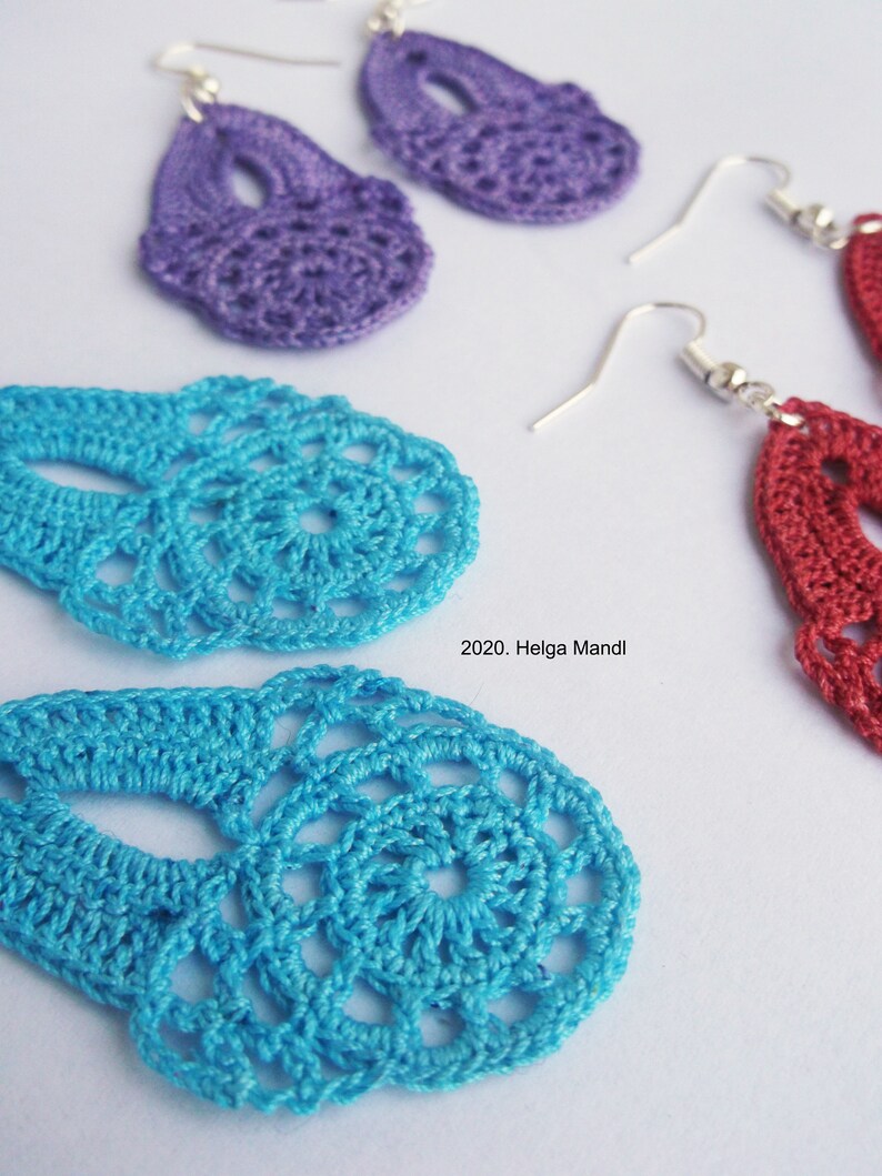Puede incluir: Primer plano de pendientes de ganchillo hechos a mano en tonos morado, turquesa y rojo. Los pendientes tienen un dise&ntilde;o delicado y calado con ganchos plateados. La imagen incluye el texto "2020. Helga Mandl".