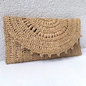 May include: A beige woven clutch bag. The bag has a flap with a semi-circular design and a scalloped edge. The clutch is made from a straw-like material, ideal for a summer accessory. The bag is approximately 30 cm in length.