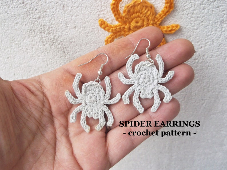 May include: A pair of crocheted spider earrings with silver hooks. The earrings are white and have a detailed design. The text "SPIDER EARRINGS - crochet pattern -" is visible below the earrings.