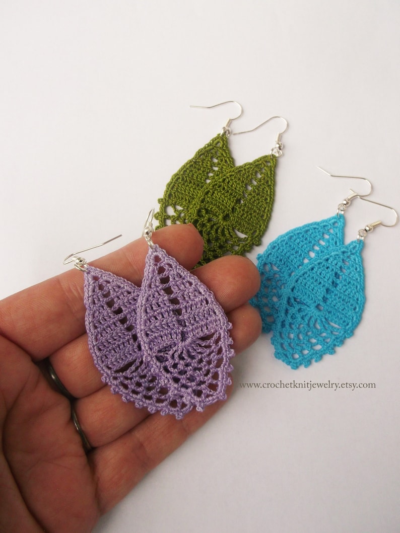 May include: A pair of crocheted earrings in purple, green, and blue. The earrings are shaped like teardrops and have a delicate, lacy design.