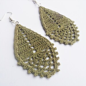 May include: A pair of green crochet earrings with a teardrop shape. The earrings are made with a delicate, lacy pattern.