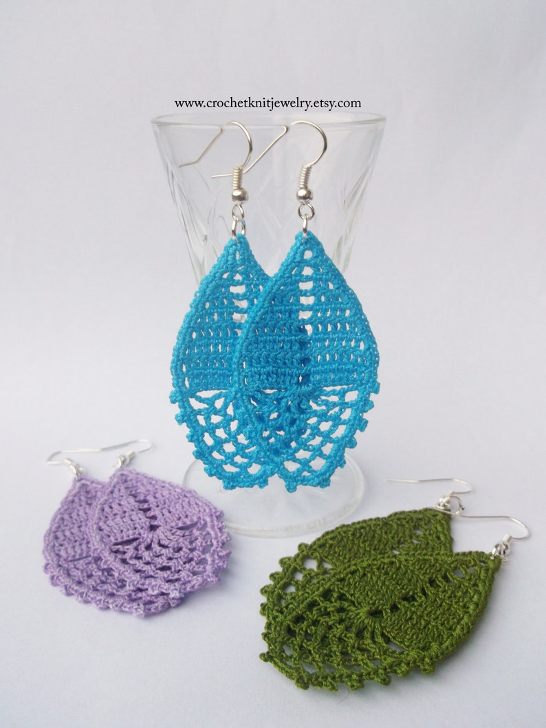 May include: Three pairs of crocheted teardrop-shaped earrings in turquoise, lavender, and olive green. The earrings are handmade and feature a delicate, lacy design.